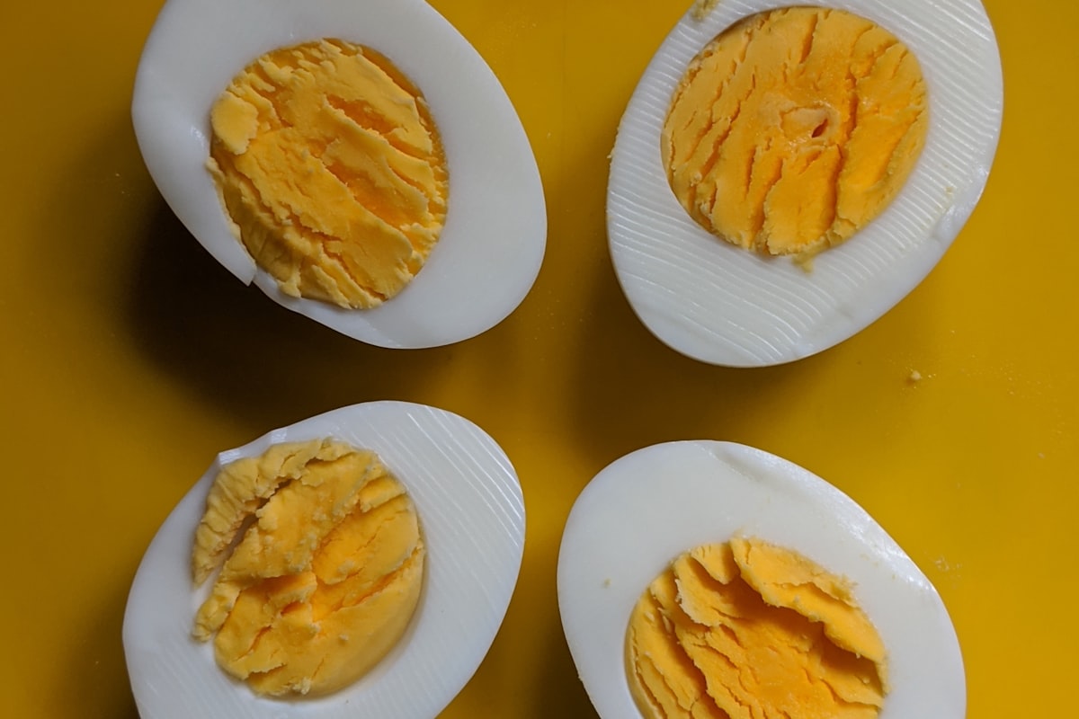 Halved boiled eggs showing fully cooked yellow yolks on a yellow background