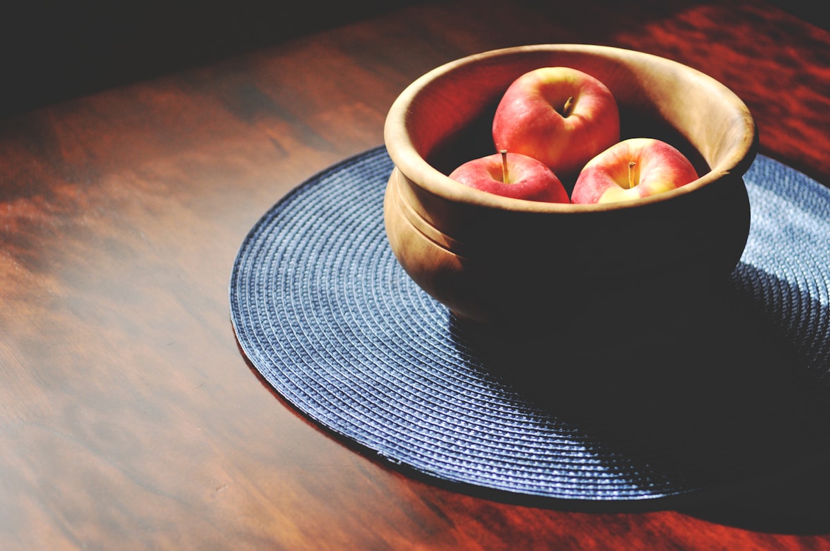 Bowl of ripe apples on a wooden kitchen table, the kind of fruit that attracts fruit flies