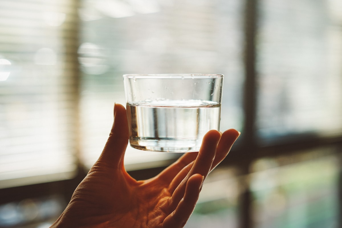 Hand holding a glass of water against a bright window