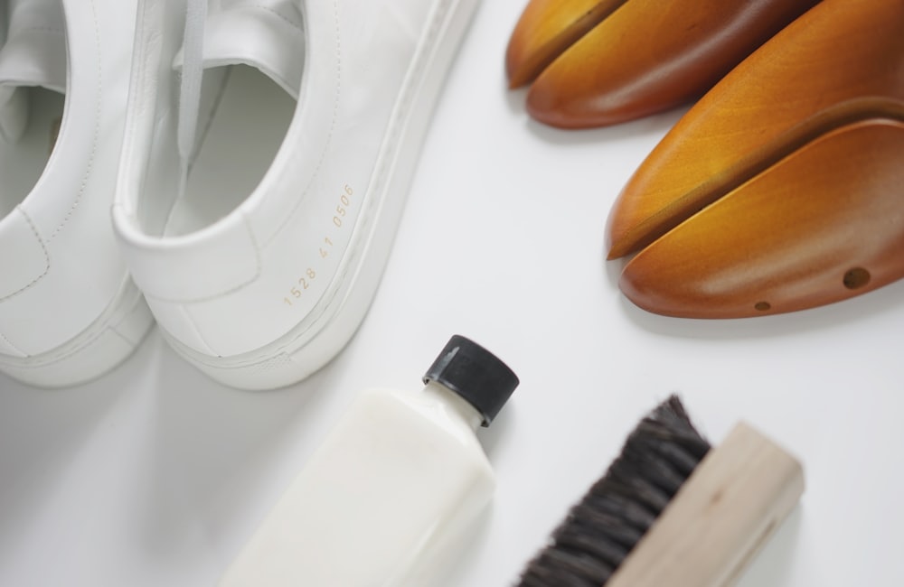 A pair of white sneakers next to a cleaning bottle and brush